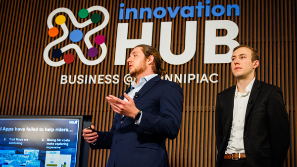 2 male students speaking in front of the Innovation Hub logo