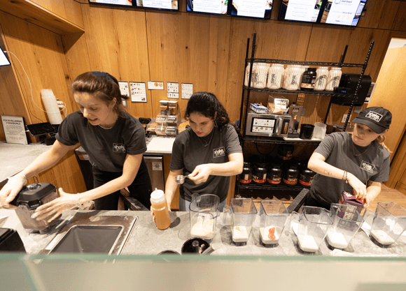 Three student employees make smoothies in a handful of blenders at the Shake Smart counter