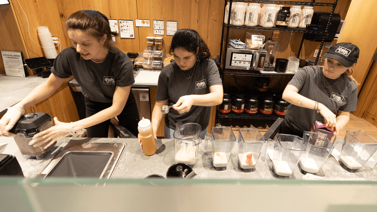 Three student employees make smoothies in a handful of blenders at the Shake Smart counter
