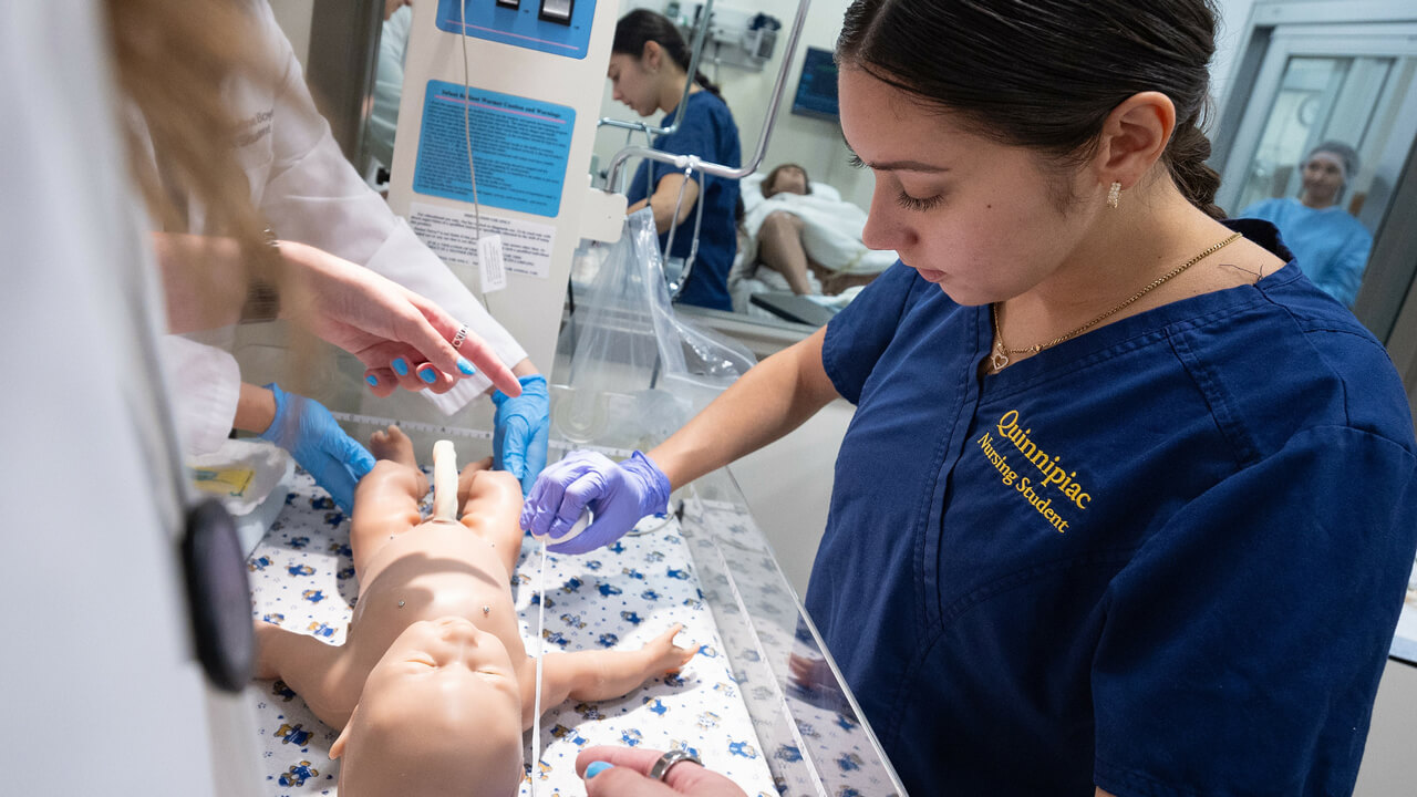 A nursing student tends to an infant mannequin during a birthing simulation.