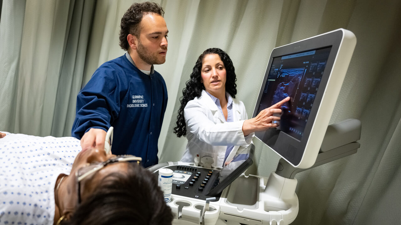 A medical student receives direction from a professor while using digital imaging equipment to examine a patient.