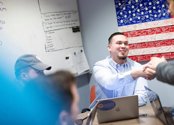 Navy veteran Colby Milliken ’21, economics and business management major, sitting at a table shaking hands with Retired Col. Kelly Wolgast in the veterans’ lounge in the Center for Communications and Engineering