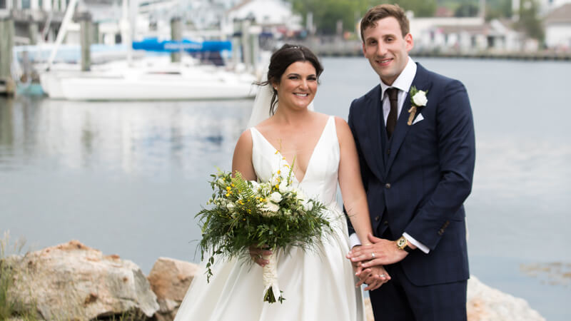 Nicole Howe and Jonathan Hayes hold hands at a water front on their wedding day