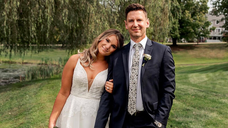 Sarah Pandolfi leans on the shoulder of Robin Schuppert under a tree on their wedding day