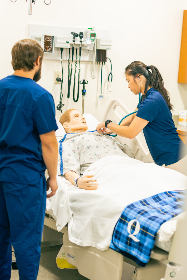 Physical therapy students tend to a mannequin patient in a simulation hospital environment.