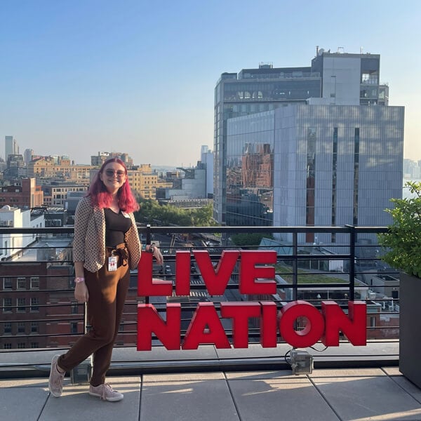 Student intern posing next to Live Nation sign with NYC skyline in the background