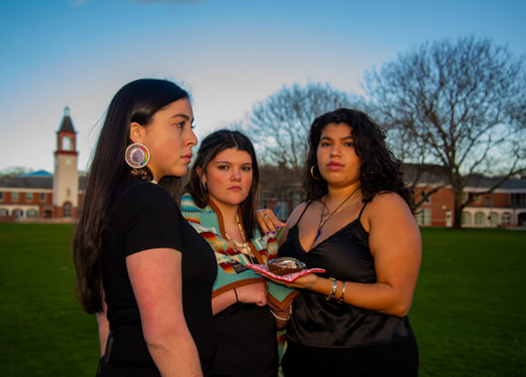 3 female students of QU's Indigenous Student Union holding Indigenous items