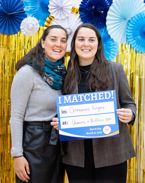 Christine Etzel poses for a photo with her sister in front of a golden backdrop