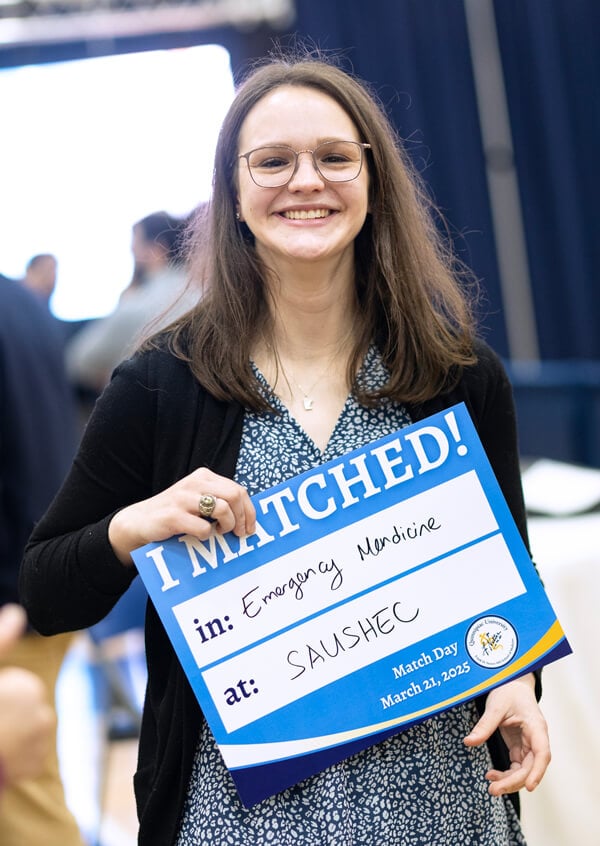 Tara Kobayashi holds up her sign that says she matched in emergency medicine at SAUSHEC