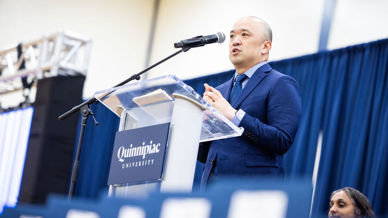 Steve Paik stands at a podium speaking to School of Medicine students and their loved ones