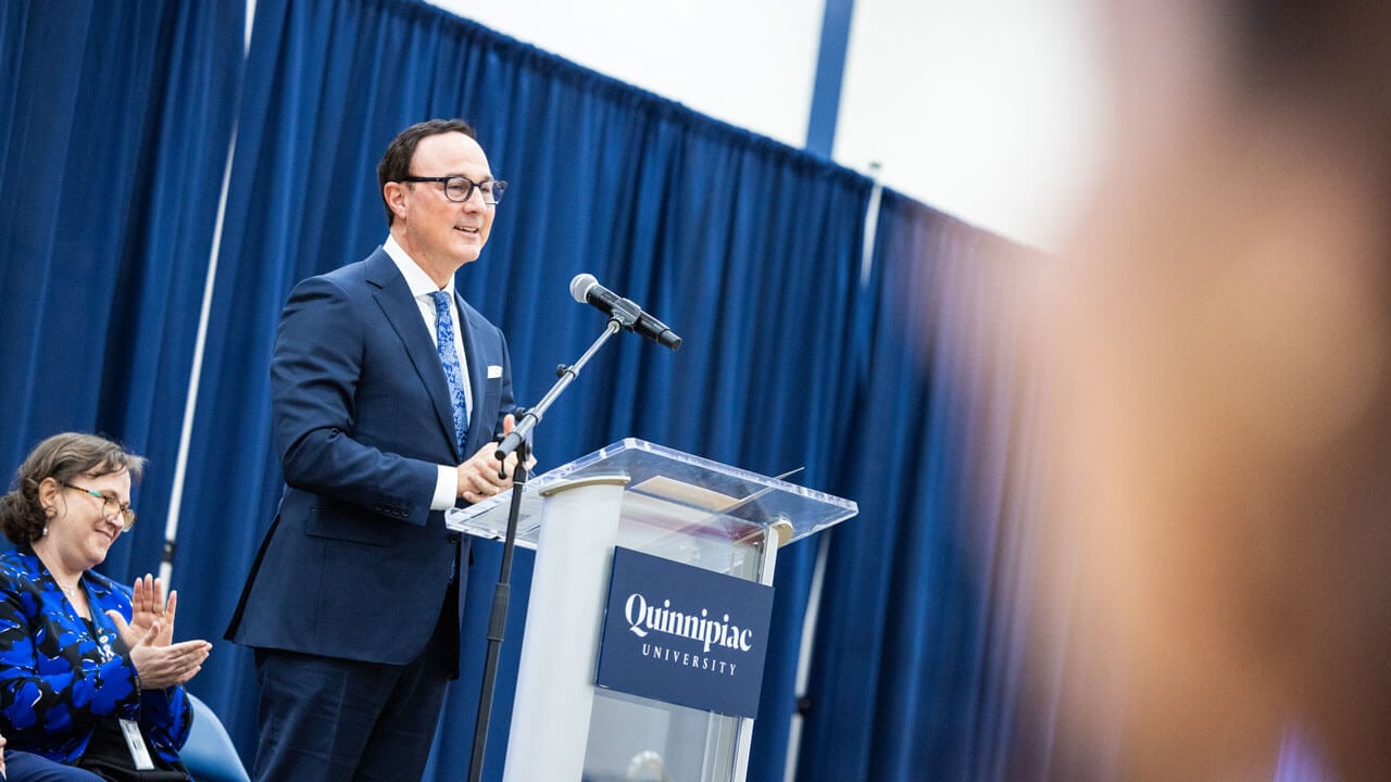 Phil Boiselle stands at a podium presenting to a crowd