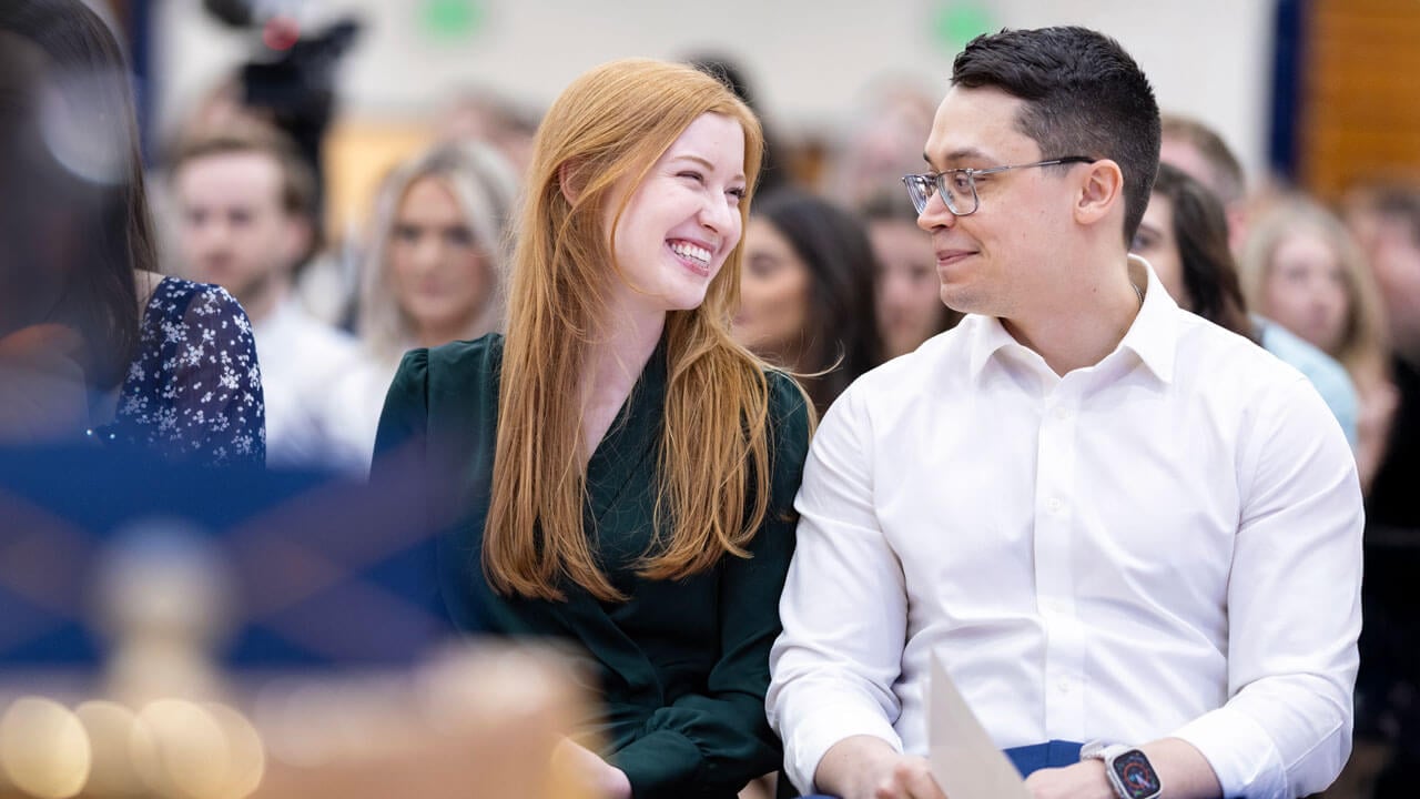 Two School of Medicine students smile at each other while sitting down waiting for their placements