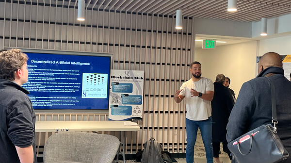 A male student presenting at a conference, gesturing at a screen