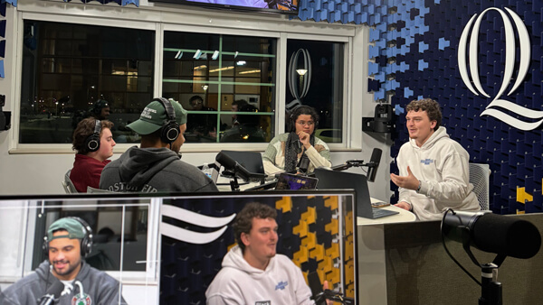 a group of 4 male students sitting around a podcasting table with microphones and headphones