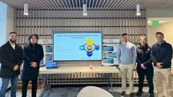 5 male students posing in front of a presentation on a screen