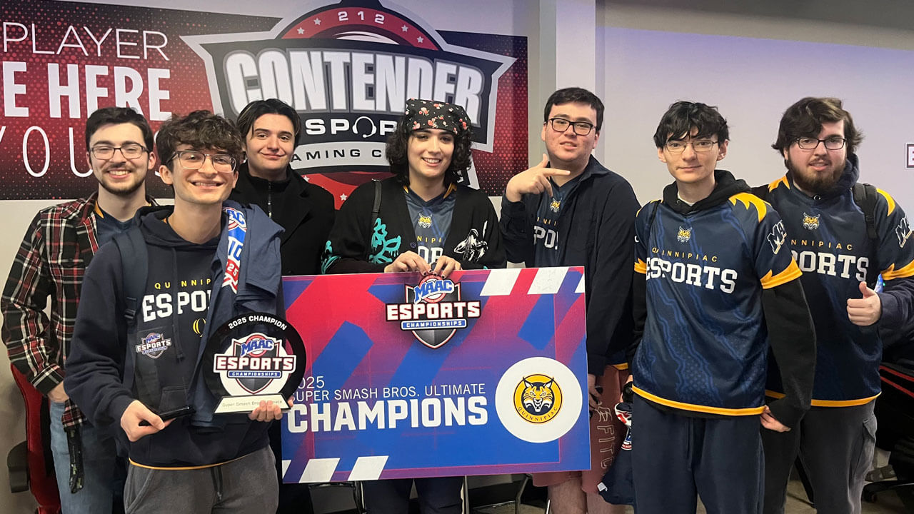 Quinnipiac eSports team poses and smiles with a championship poster.