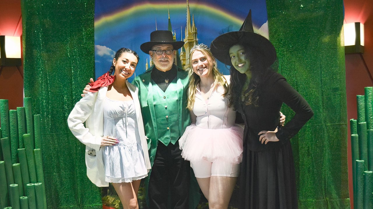 Participants pose for a photo in their costumes in front of a rainbow backdrop.