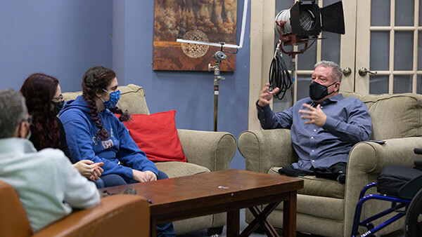 Dave Stevens speaks to 2 students sitting on a couch.