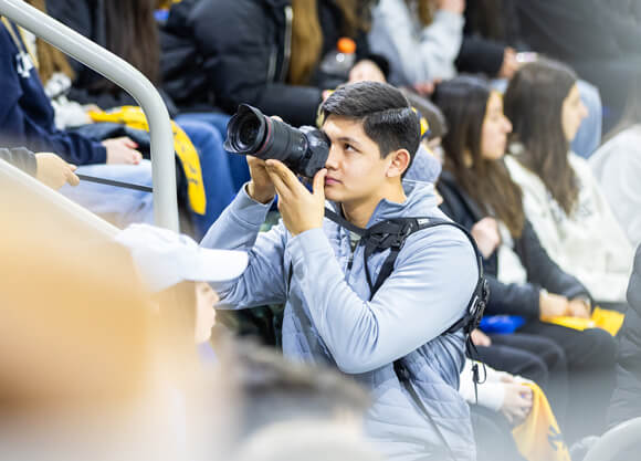 A Quinnipiac student employee takes a photo during a hockey game