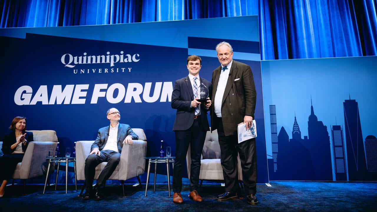 Two individuals smile for a photo on stage while holding an award.