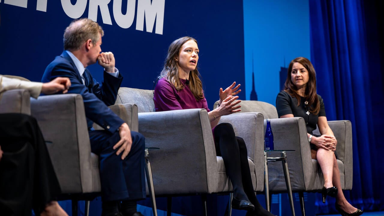 Panelists speak on a stage while sitting in chairs.