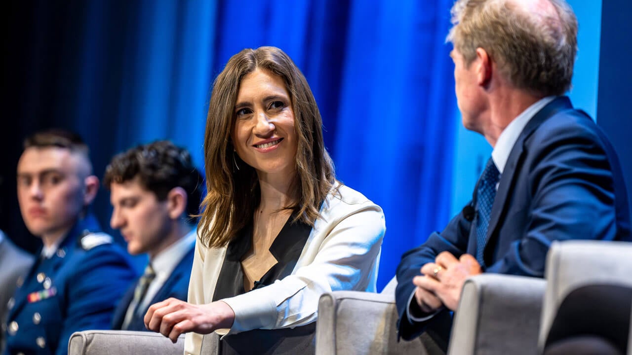 Panelists look at each other and discuss while sitting in chairs.