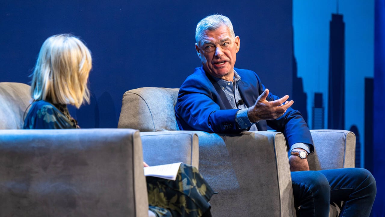 Two individuals speak to each other on a stage.