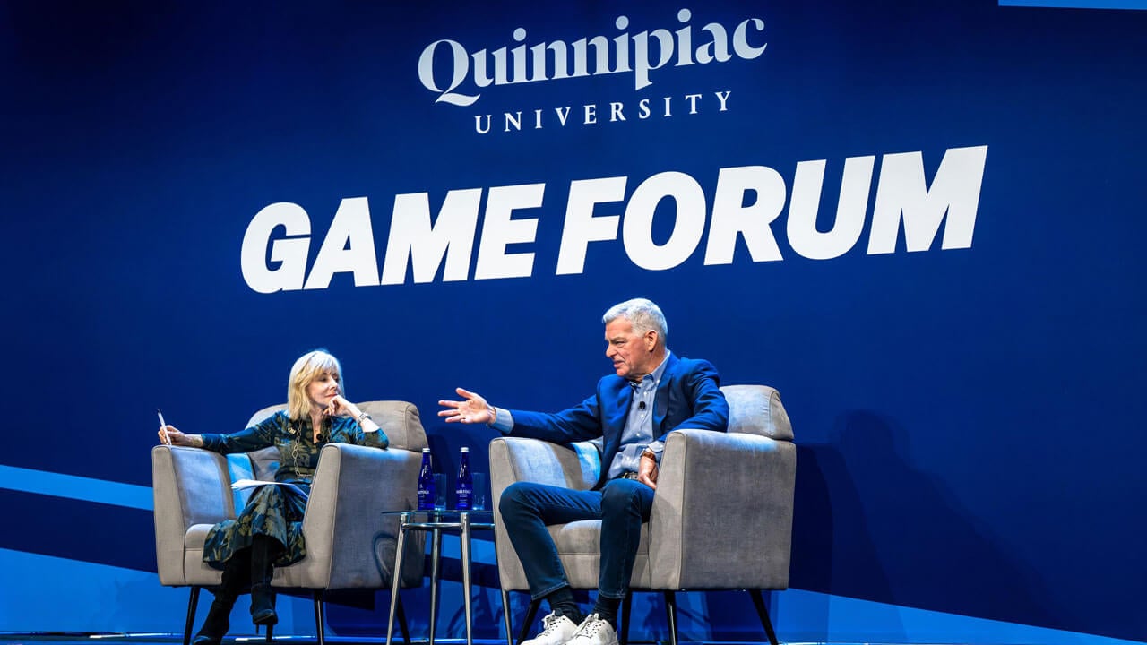 Two individuals sit in chairs on stage at GAME Forum.