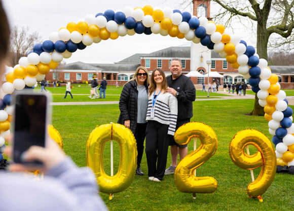 Family smiles for a photo at Admitted Students Day in front of the Arnold Bernhard Library.