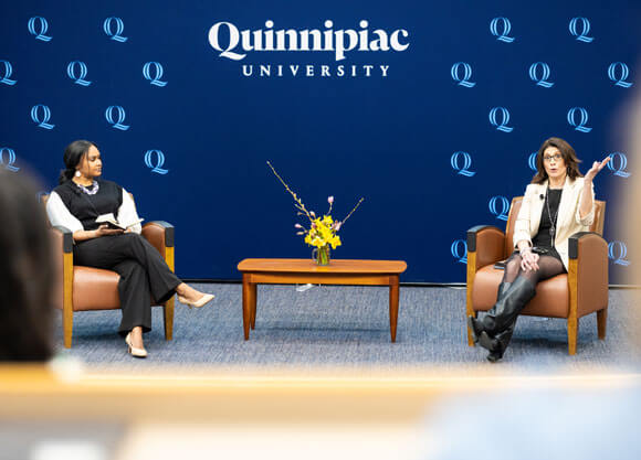 Two individuals sit in chairs and discuss with each other.