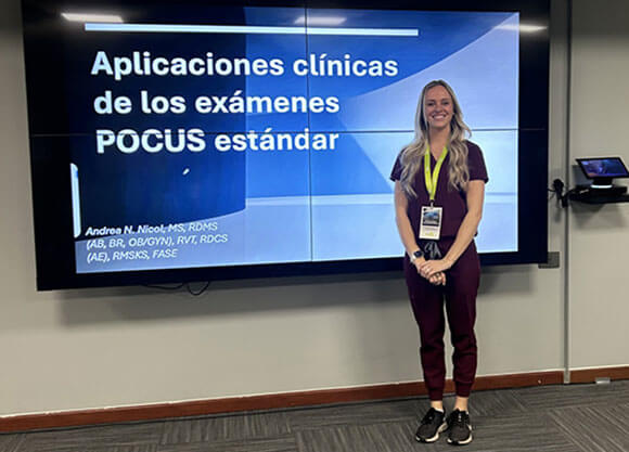Andrea Nicol stands in front of a digital screen showing her presentation