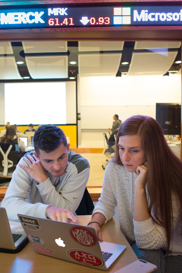 2 students work on their laptops in the study room outside the Financial Technology Center.