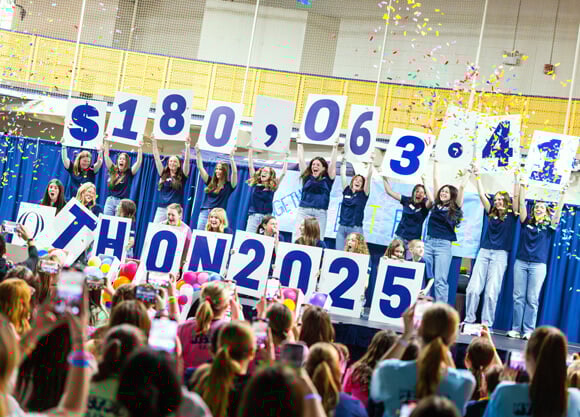 Students cheer and confetti flies as they hold up signs reading the total raised for QTHON as $180,063.41