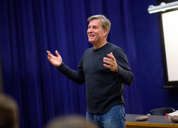 A man stands at the front of a room talking to students.