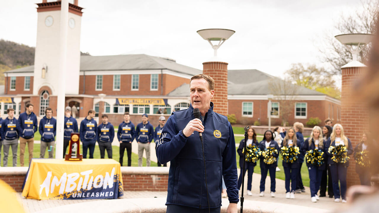 Men's ice hockey coach Rand Pecknold speaking to the crowd
