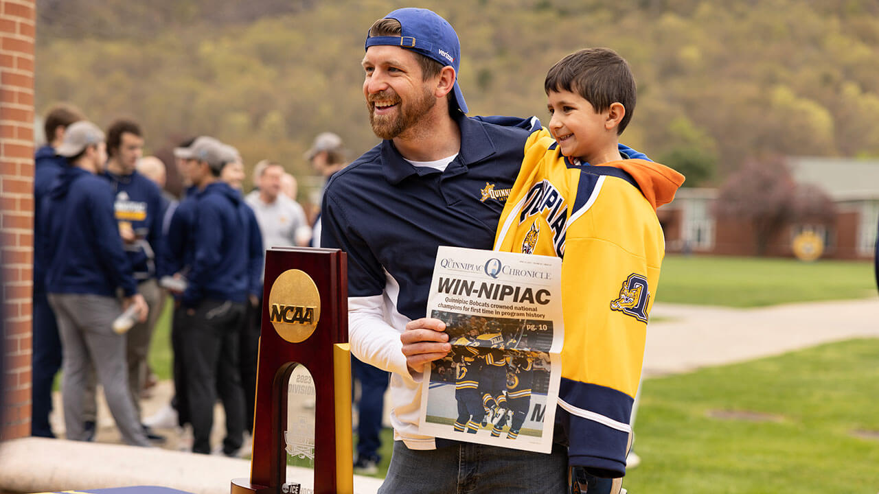 Spectators pose in front of the NCAA National Championship trophy