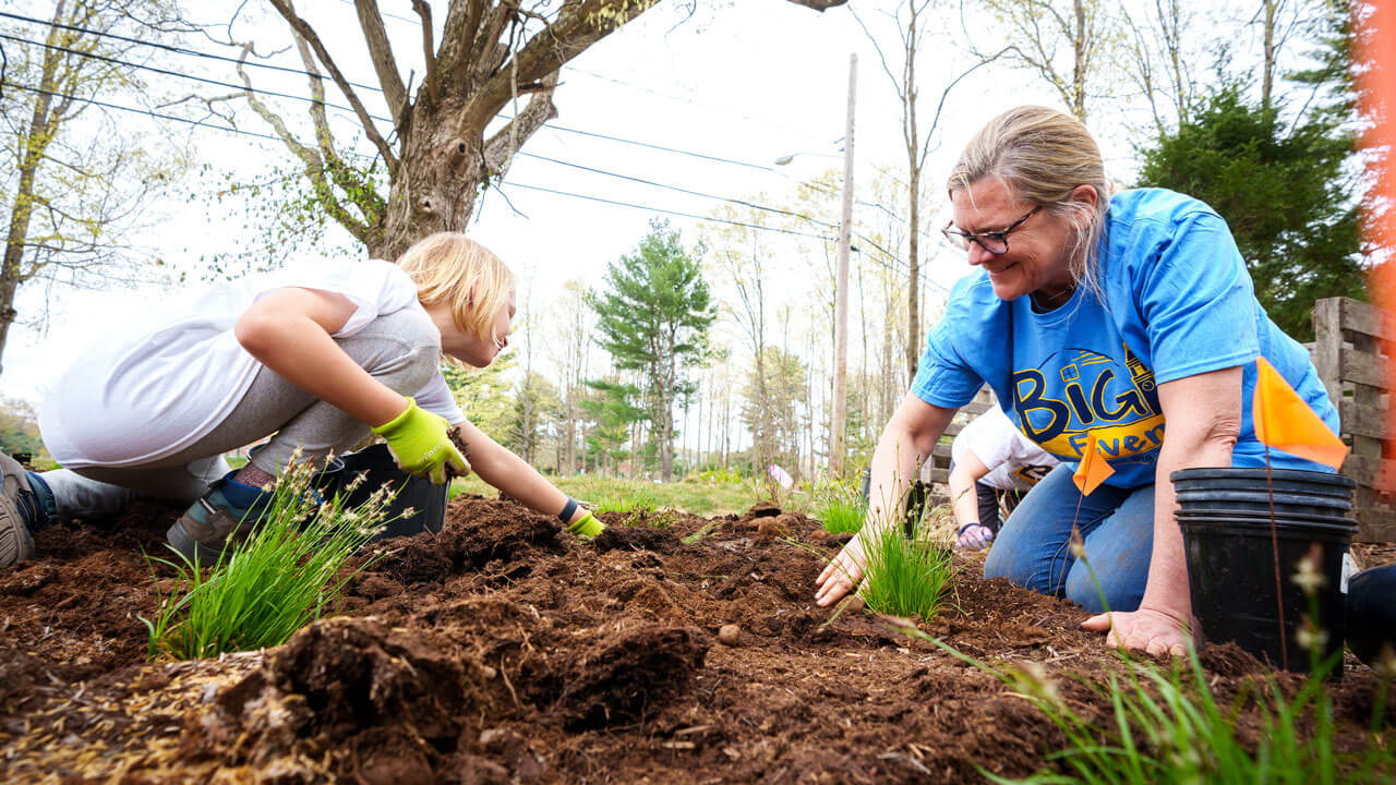 Professor Nancy Burns weeding a garden with a student