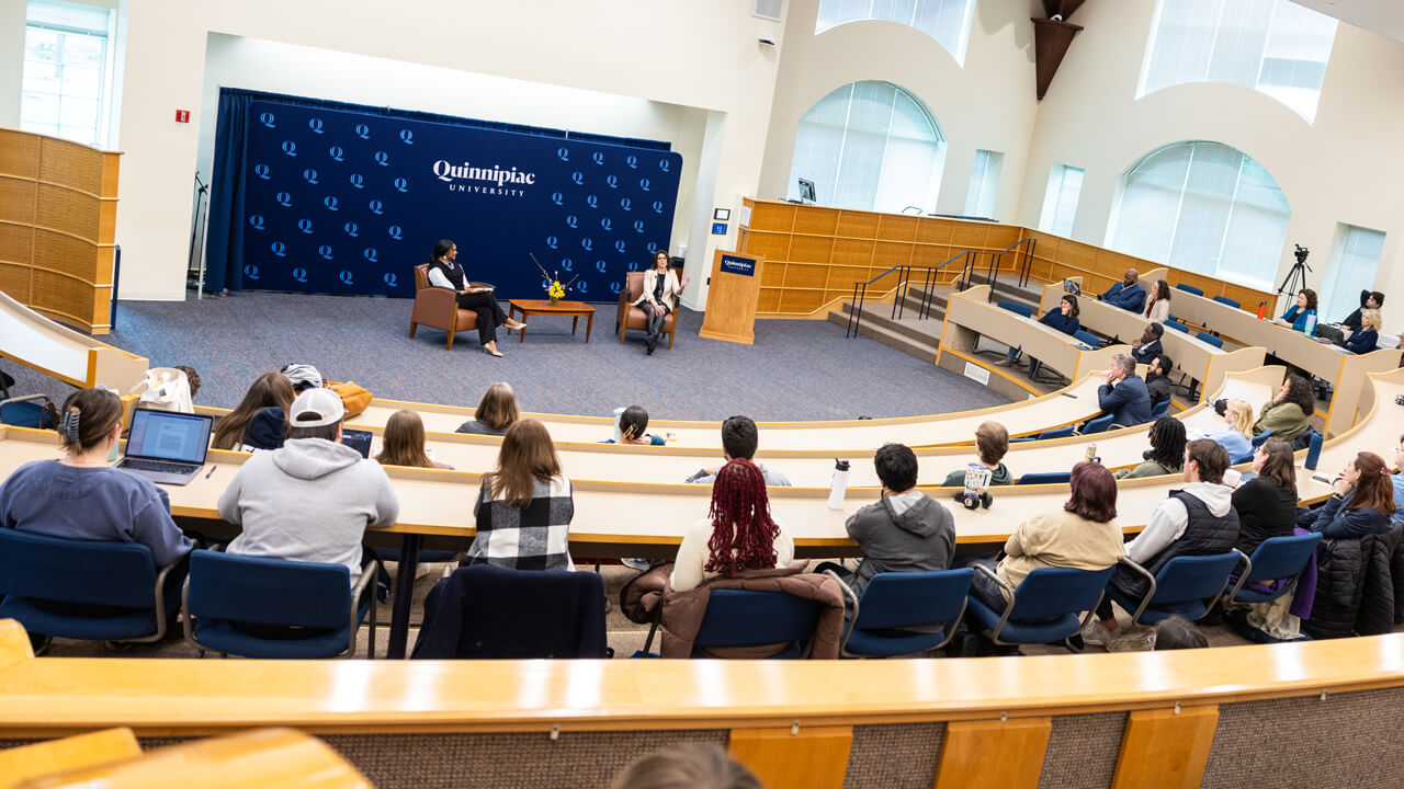 2 women seated in comfy chairs talking to a crowd of seated people in an auditorium