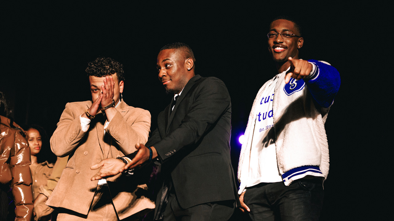 Students smiling, clapping and pointing at camera on stage at fashion show