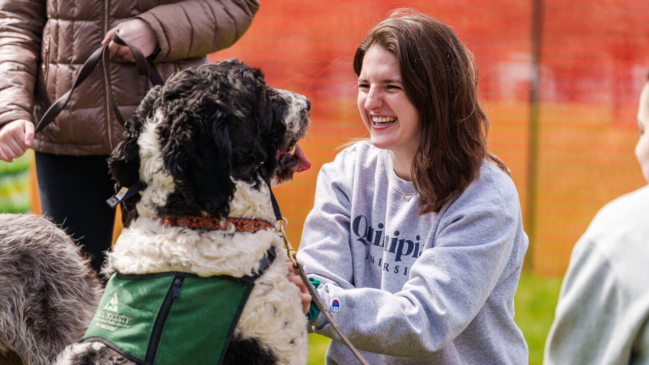 Girl petting black and white dog while smiling and laughing