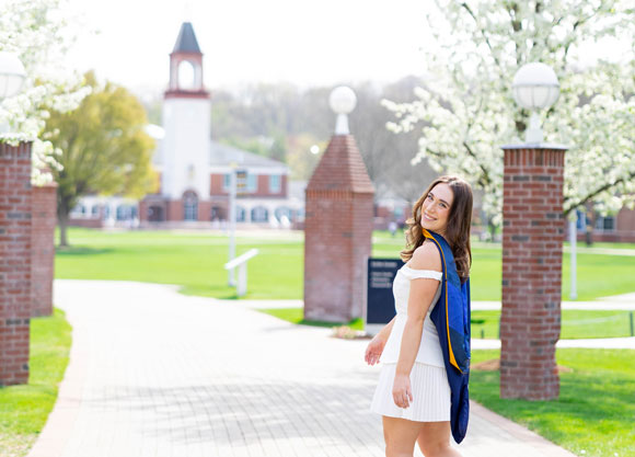 Photo of a student walking on campus with the Arnold Bernhard Library in the background.