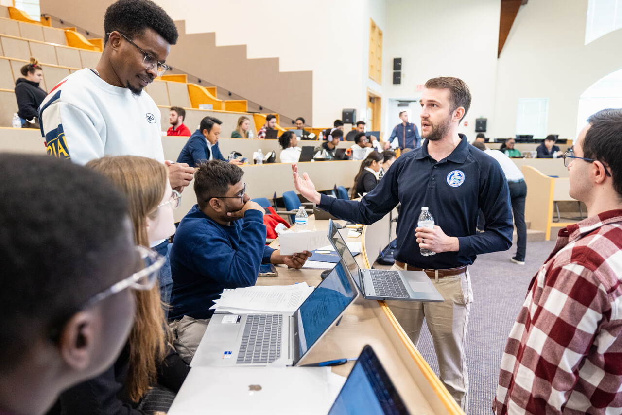 Students receive instruction while working on computers in a collaborative group setting.