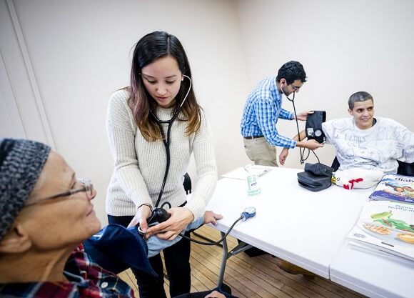 Dunbar takes the blood pressure of a woman as student takes a man's blood pressure behind her.