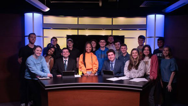 A group of students stands behind the desk on the new Q30 Television set