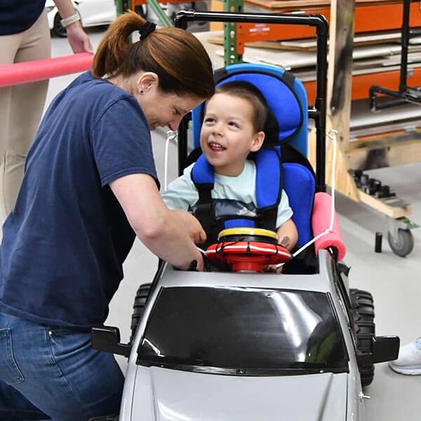 An adult fastening a child into a motorized toy car.