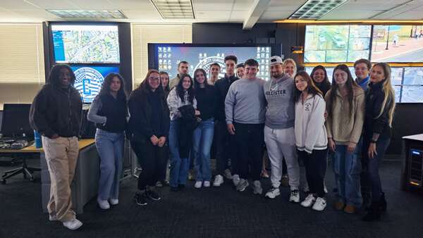 Students a part of CJ 200 posing for a group photo in front of screens at Hartford Police Department's C4 Center
