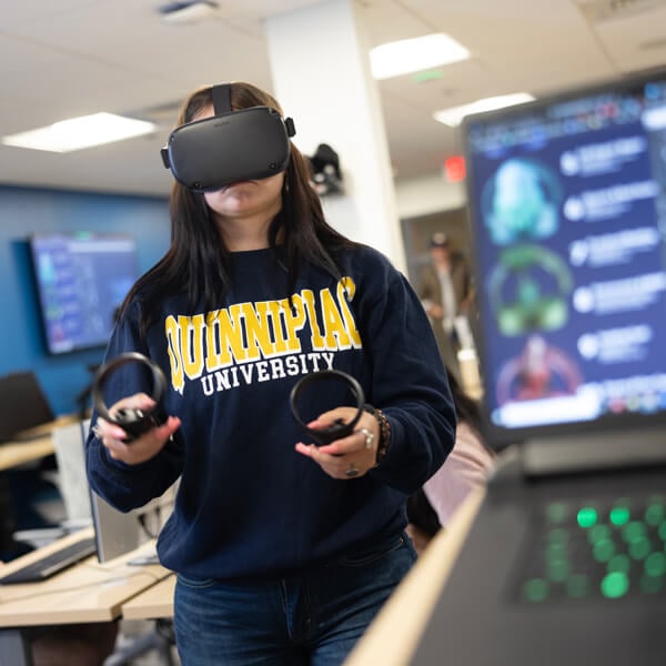 A student who is wearing a VR headset and holding controllers tests a VR game