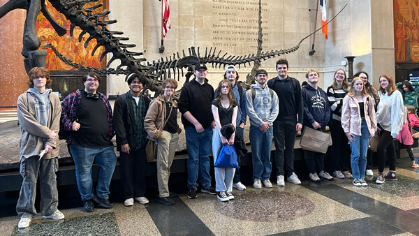 A group of first-year students posing in front of a dinosaur skeleton at the American Museum of Natural History in NYC.