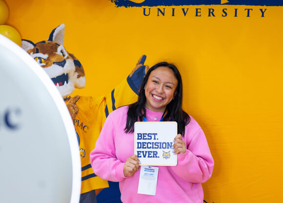 A newly admitted student smiles for a photo holding a sign that says "Best Decision Ever"