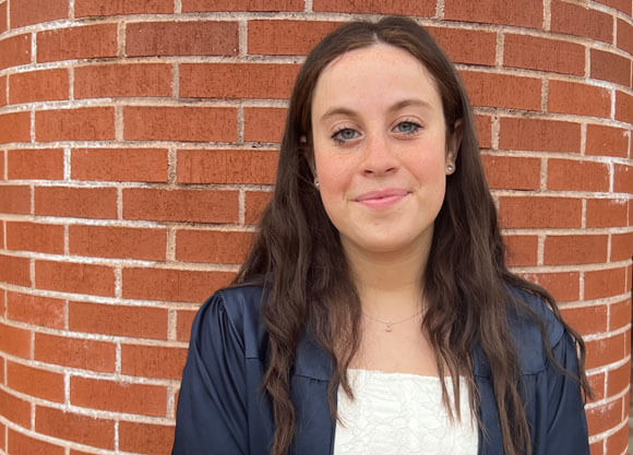 Morgan Murray softly smiles wearing a white dress and navy graduation gown.